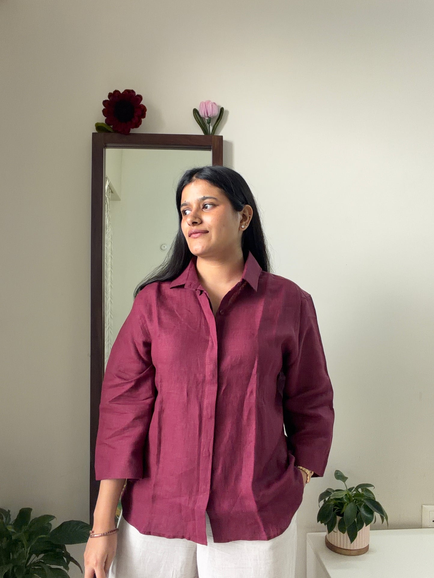 A woman wearing a 3/4th-sleeve button-up linen shirt in a burgundy or berry color, paired with beige pants
