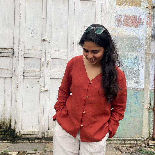 Woman wearing a cinnamon color top and white pants standing in front of a weathered wall.